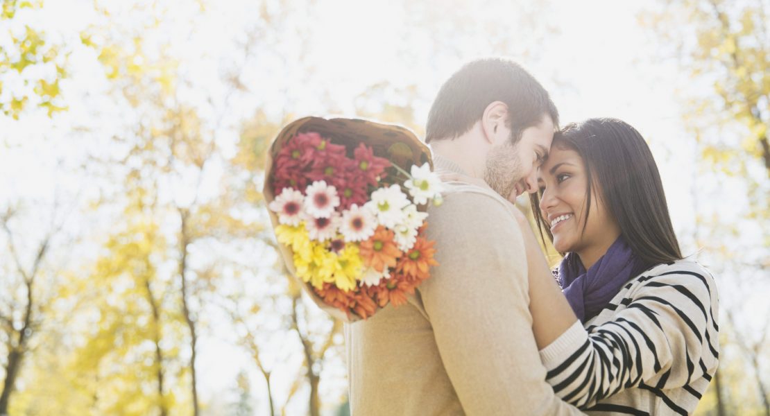 Um casal se abraçando com um buquê de flores após um pedido de namoro criativo.