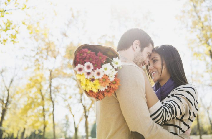 Um casal se abraçando com um buquê de flores após um pedido de namoro criativo.