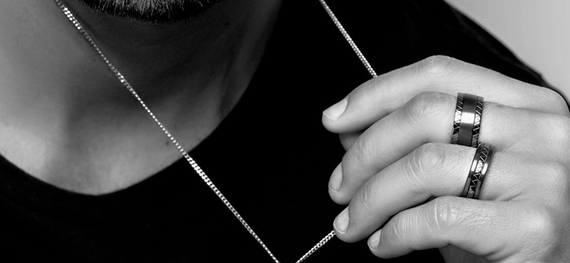 Imagem em preto e branco um homem segurando um colar e usando anel masculino