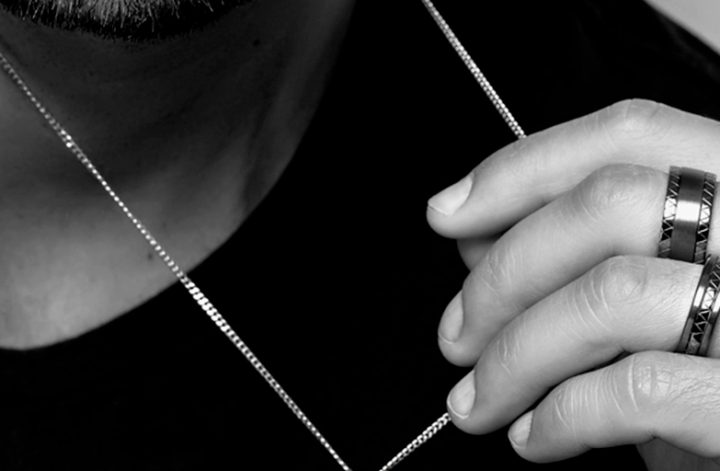 Imagem em preto e branco um homem segurando um colar e usando anel masculino