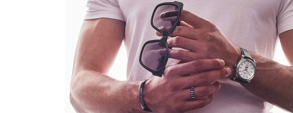 Homem com óculos de sol na mão e outros acessórios masculinos( anel, pulseira e relógio vivara.).
