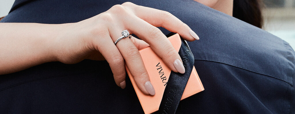 Na imagem um casal, mulher usando anel vivara e segurando caixa de presente pequena.