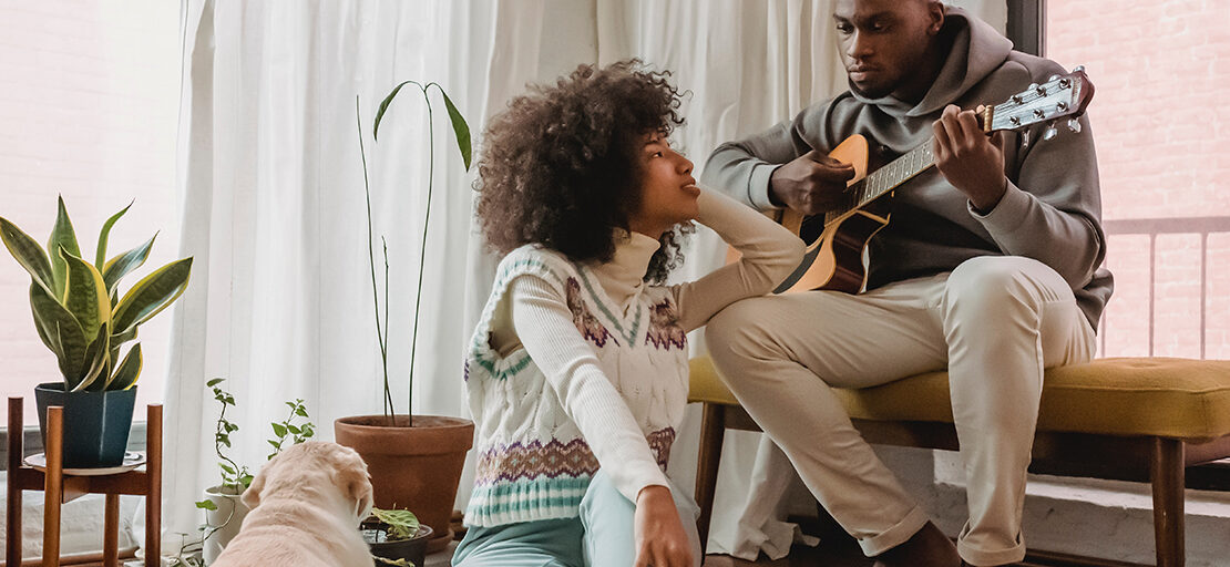 na imagem, um casal está se olhando, enquanto o homem toca violão para sua namorada.