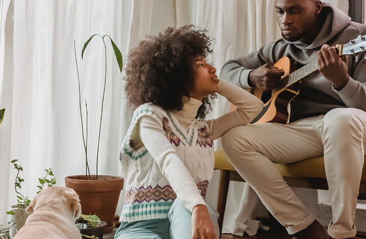 na imagem, um casal está se olhando, enquanto o homem toca violão para sua namorada.