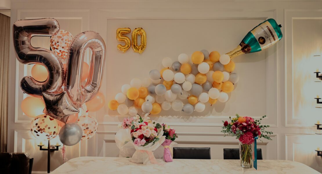 painel comemorativo de bodas de ouro com balões e mesa com arranjos de flores