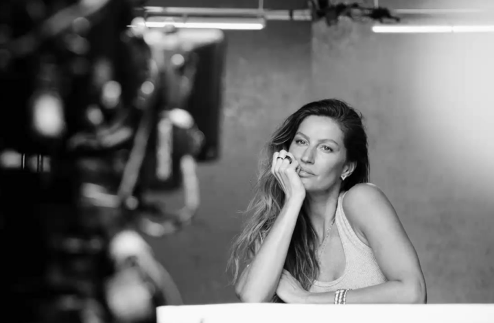 Imagem em preto e branco capturada durante o making of da campanha de Dia das Mães da Vivara. A Gisele Bündchen está sentada, com o rosto apoiado em uma das mãos, usando uma regata clara e joias delicadas, como brincos, anéis e pulseiras que fazem parte da nova coleção de joias especial Dia Das Mães 2025.