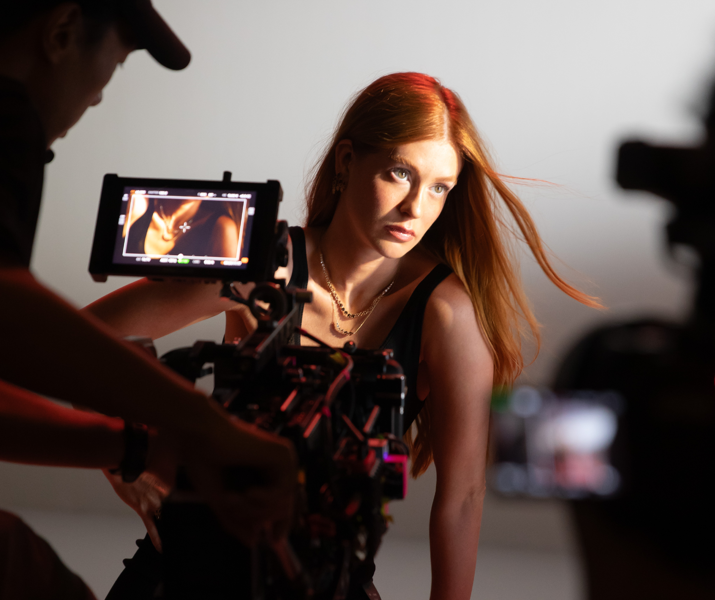 Marina Ruy Barbosa posando com confiança durante o making of da campanha de Dia das Mães Life By Vivara 2025, enquanto o fotógrafo ajusta a câmera para capturar a imagem. Ela usa joias delicadas e um look sofisticado, com os cabelos soltos e ao vento.
